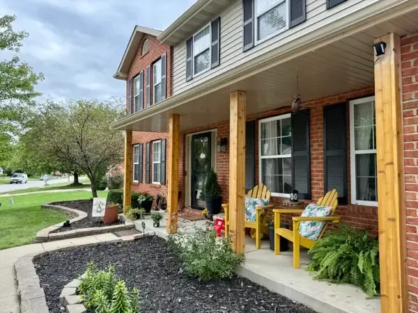 Front porch of a brick townhouse with yellow chairs, potted plants, and a landscaped walkway