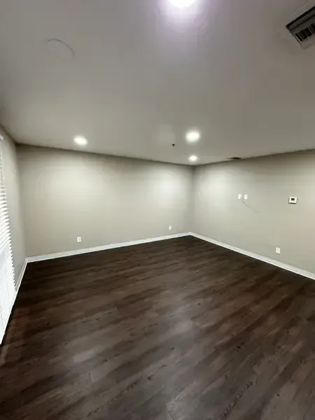 Empty beige living room with dark wood floors and recessed ceiling lights