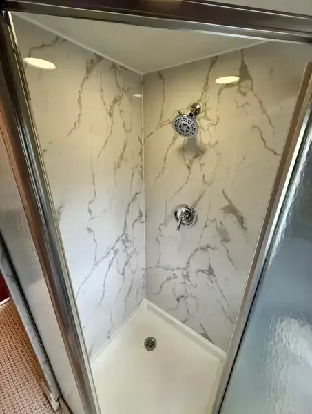 Small marble-tiled shower stall with chrome fixtures and recessed lights