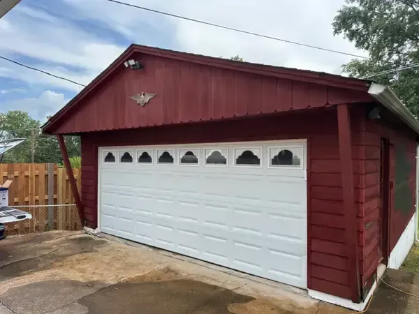 Red garage with white door and red siding in a fenced driveway
