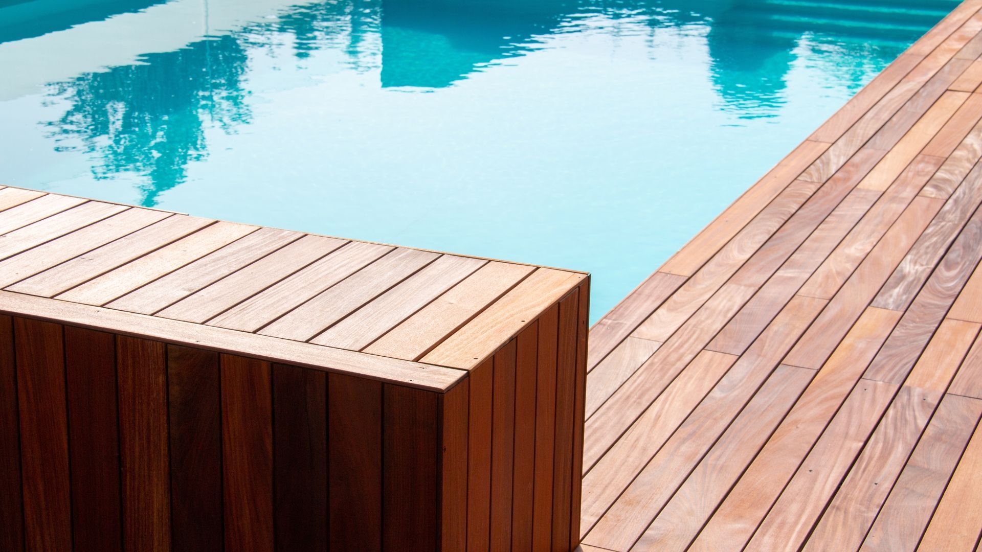 Wooden pool deck beside a turquoise swimming pool with a built-in bench seat