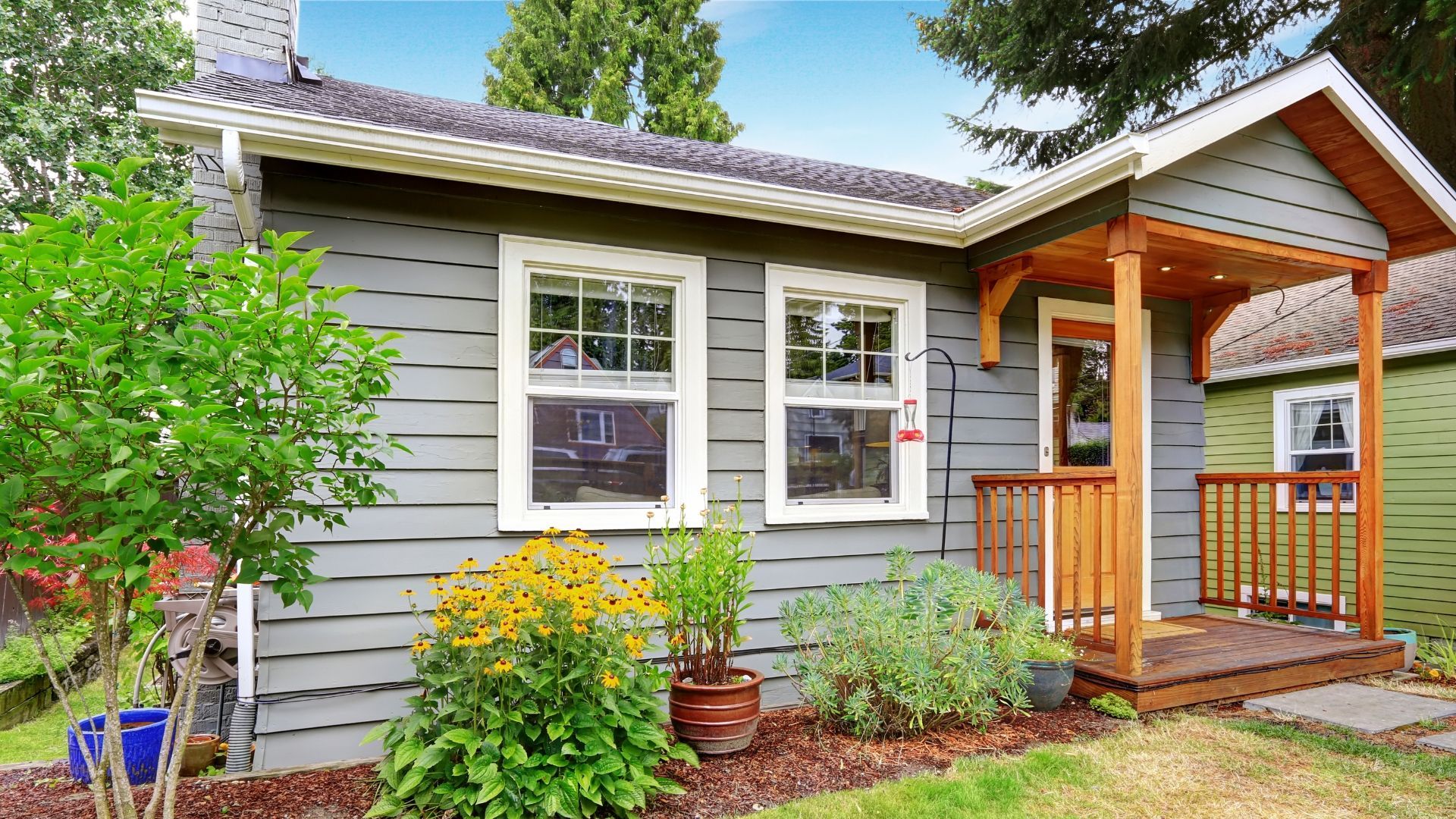 Small gray house with white-trimmed windows, orange porch, and green shrubs in front