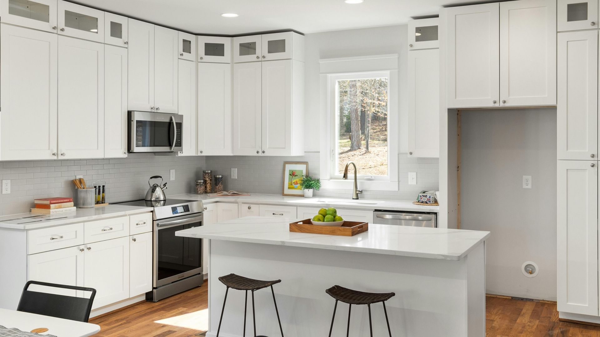 Bright white kitchen with island, stools, stainless appliances, and a window over the sink