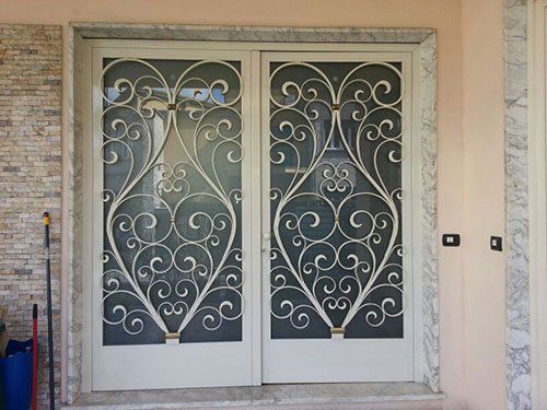 una porta finestra in vetro e legno bianco con disegni in ferro battuto