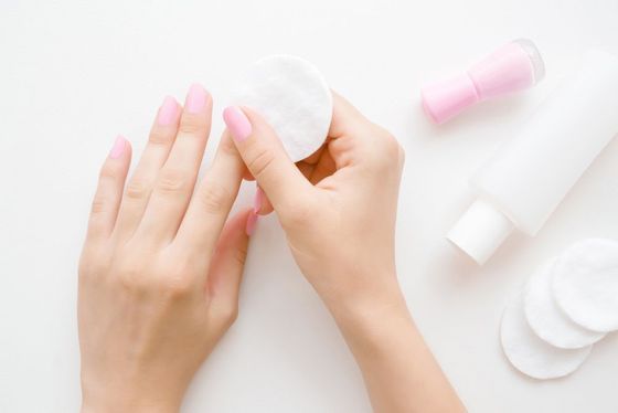 A woman is cleaning her nails with a cotton pad