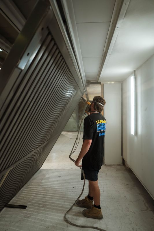 Man in a black shirt sprays a large metal gate in a white room.