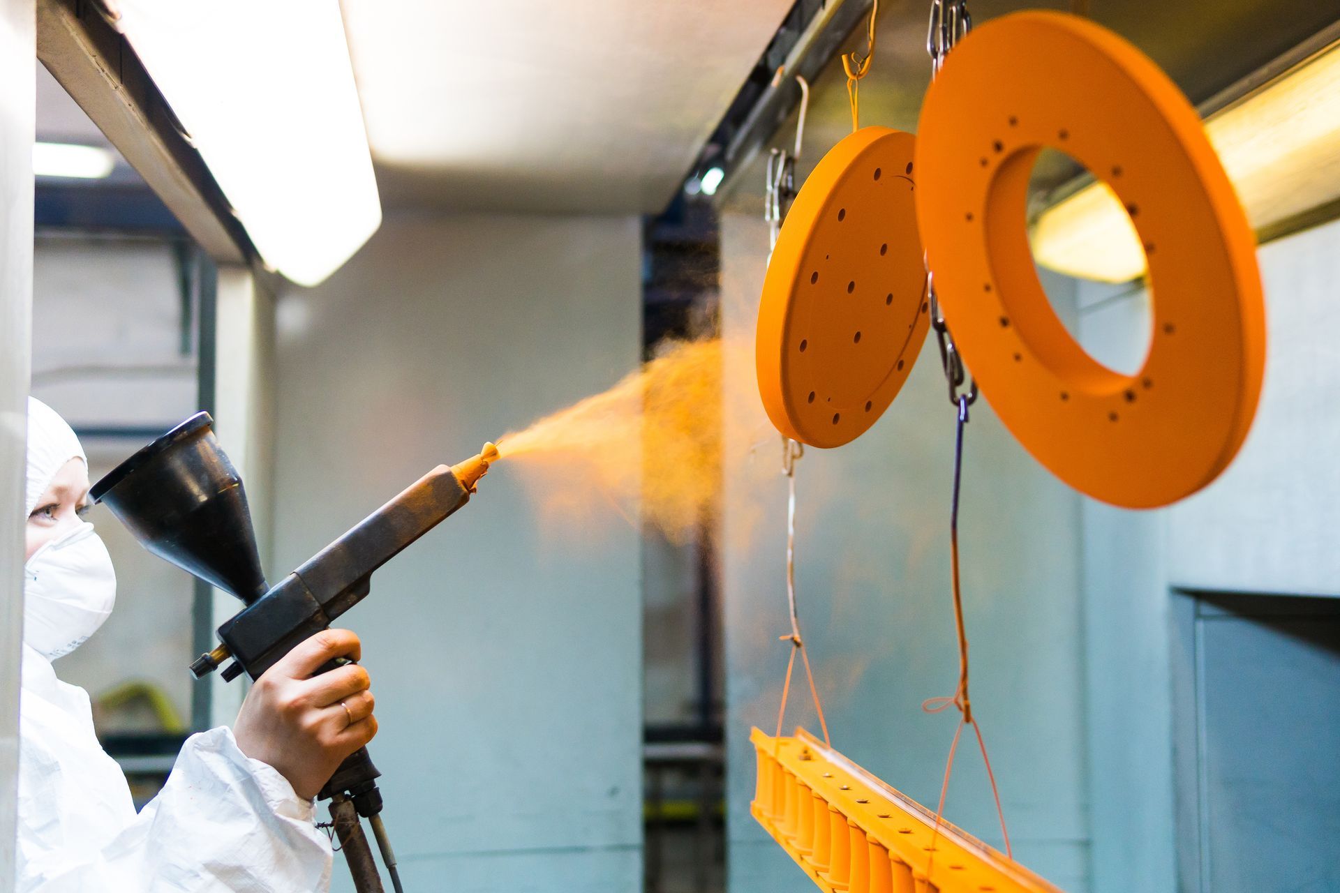 A woman in a protective suit sprays yellow powder paint from a gun on metal products. A woman in a protective suit sprays yellow powder paint from a gun on metal products.