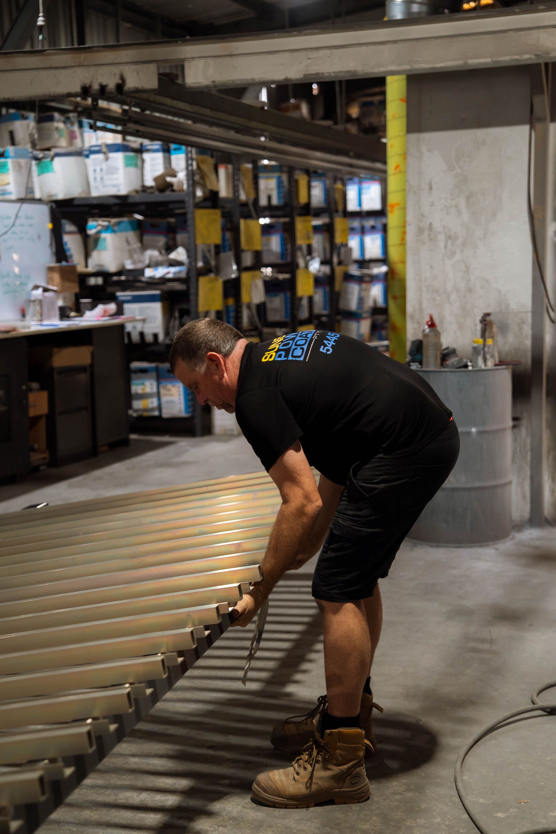 Man in black shirt and shorts working on metal structure in a workshop.