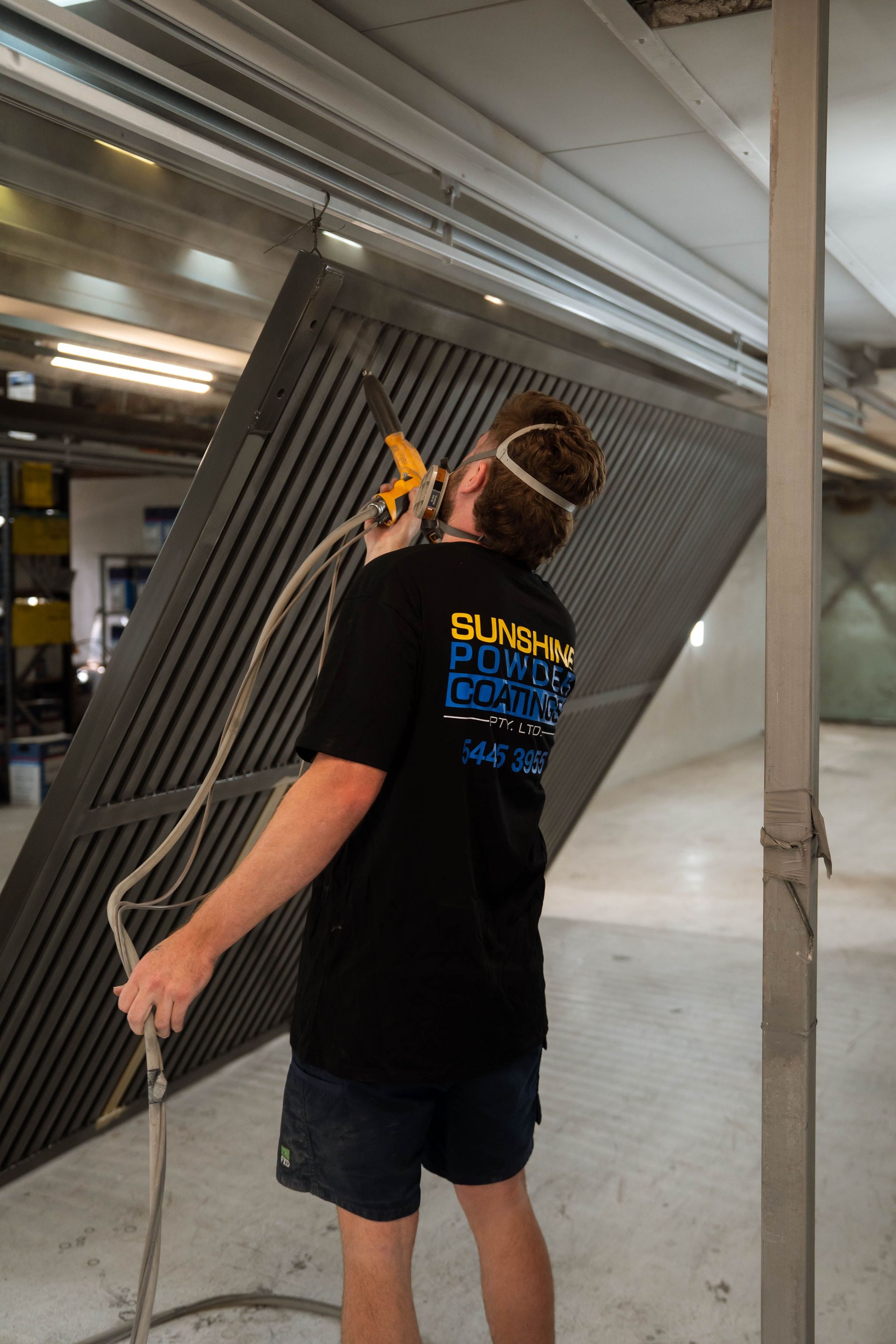 Person sprays a metal gate, wearing a mask, inside a workshop.