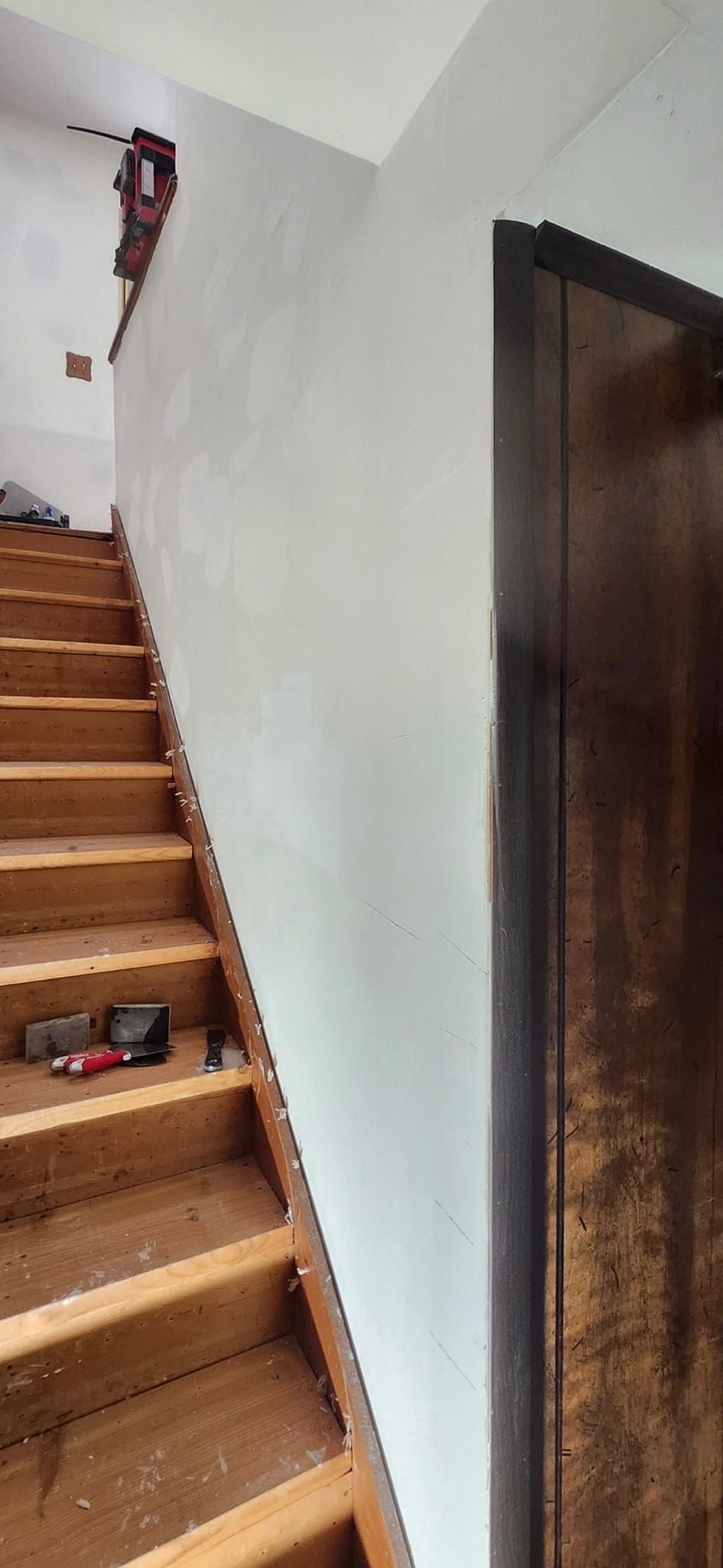 A wooden staircase leading up to a white wall next to a door.