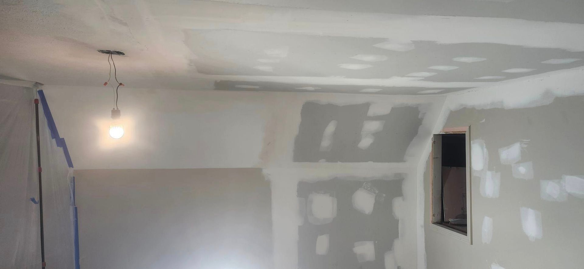 A room with drywall walls and a light hanging from the ceiling.