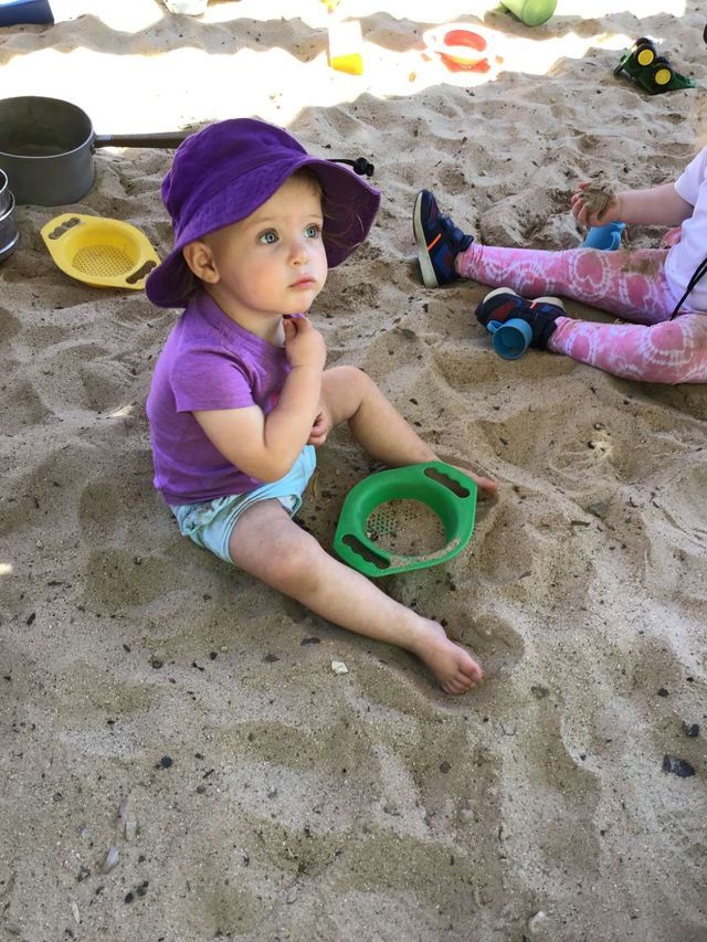A Little Girl Wearing a Purple Hat Sits in the Sand — Preschool in Coffs Harbour