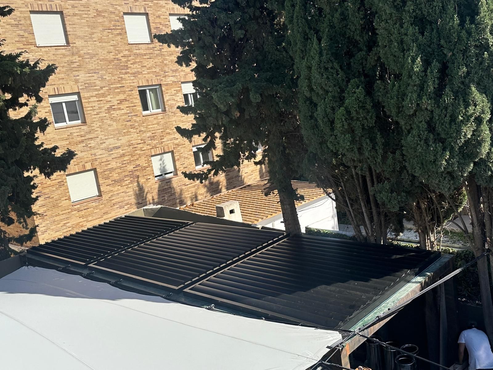 Un uomo sta lavorando su un tetto con un edificio in mattoni sullo sfondo.