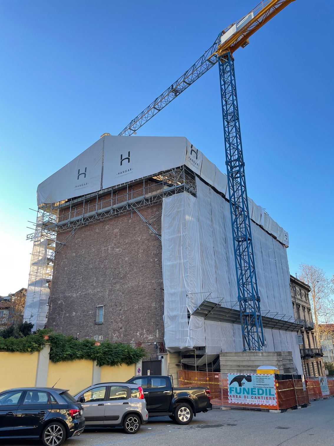 un grande edificio è coperto da impalcature e davanti ad esso sono parcheggiate le auto.
