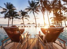 Zwei Personen sitzen bei Sonnenuntergang auf Stühlen neben einem Swimmingpool.