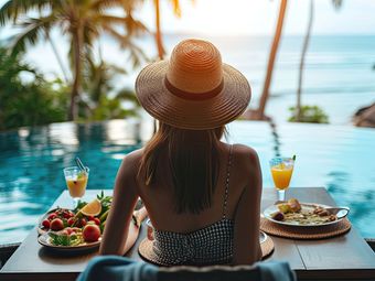 Eine Frau sitzt mit Essen und Getränken an einem Tisch neben einem Swimmingpool.