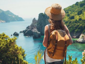 Eine Frau mit einem Rucksack steht auf einer Klippe und blickt auf den Ozean.