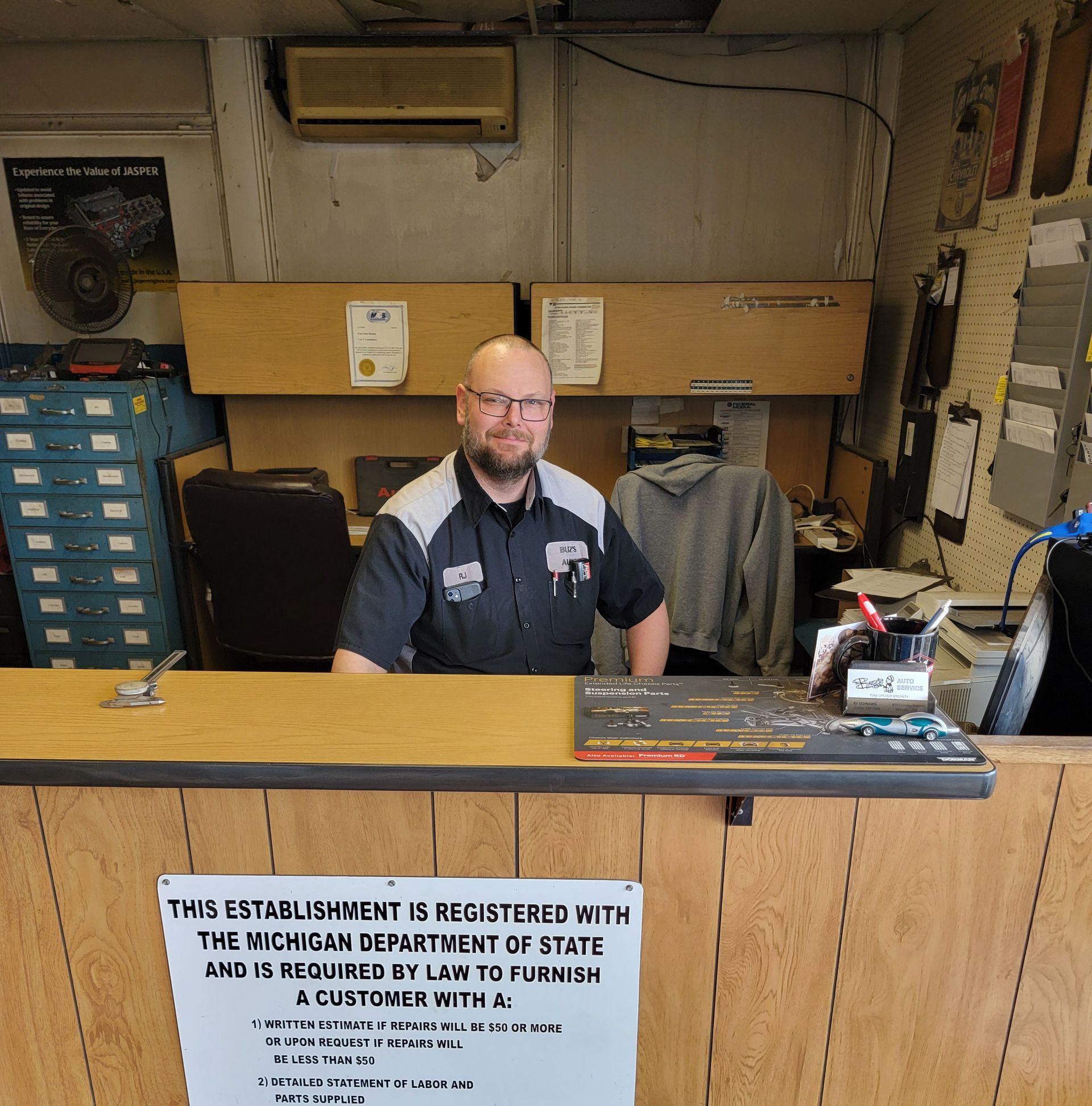 A bunch of tools are on a tray in front of a red car with the hood open.