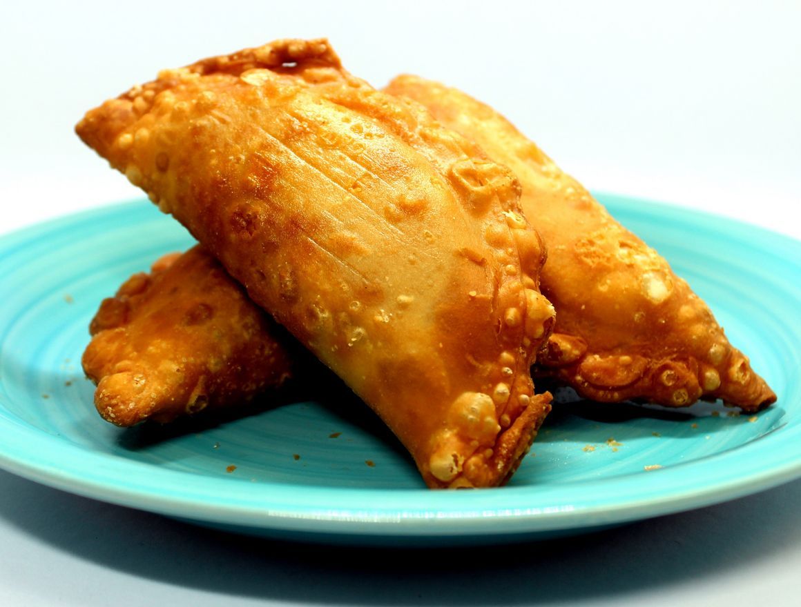 Three golden-brown, fried empanadas sit stacked on a light blue plate.