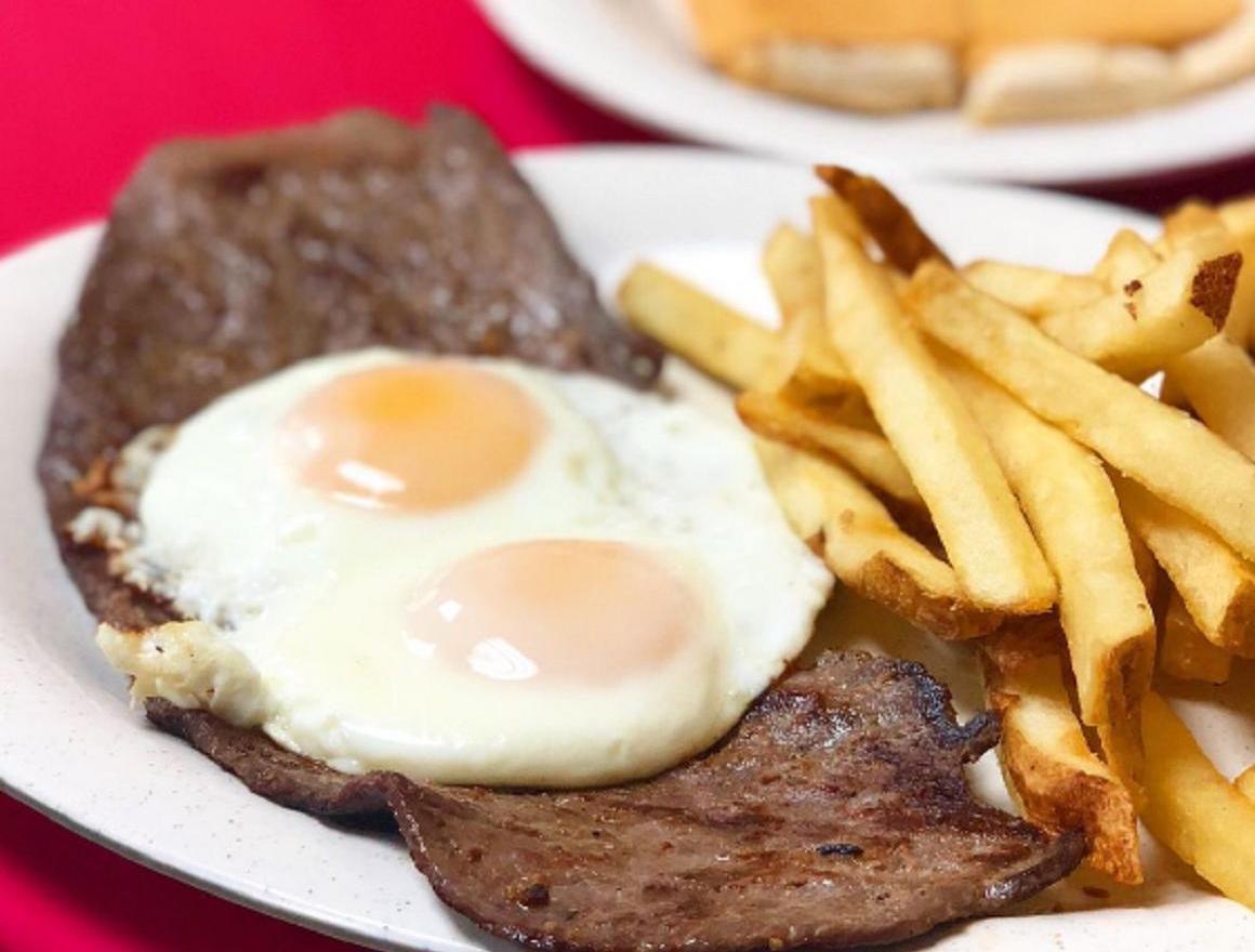 Steak, two fried eggs, and fries on a white plate; a roll is in the background.