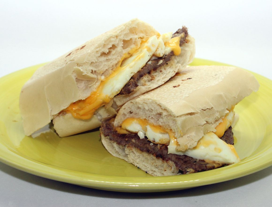 Two halves of a breakfast sandwich on a yellow plate; includes egg, meat, and cheese on bread.