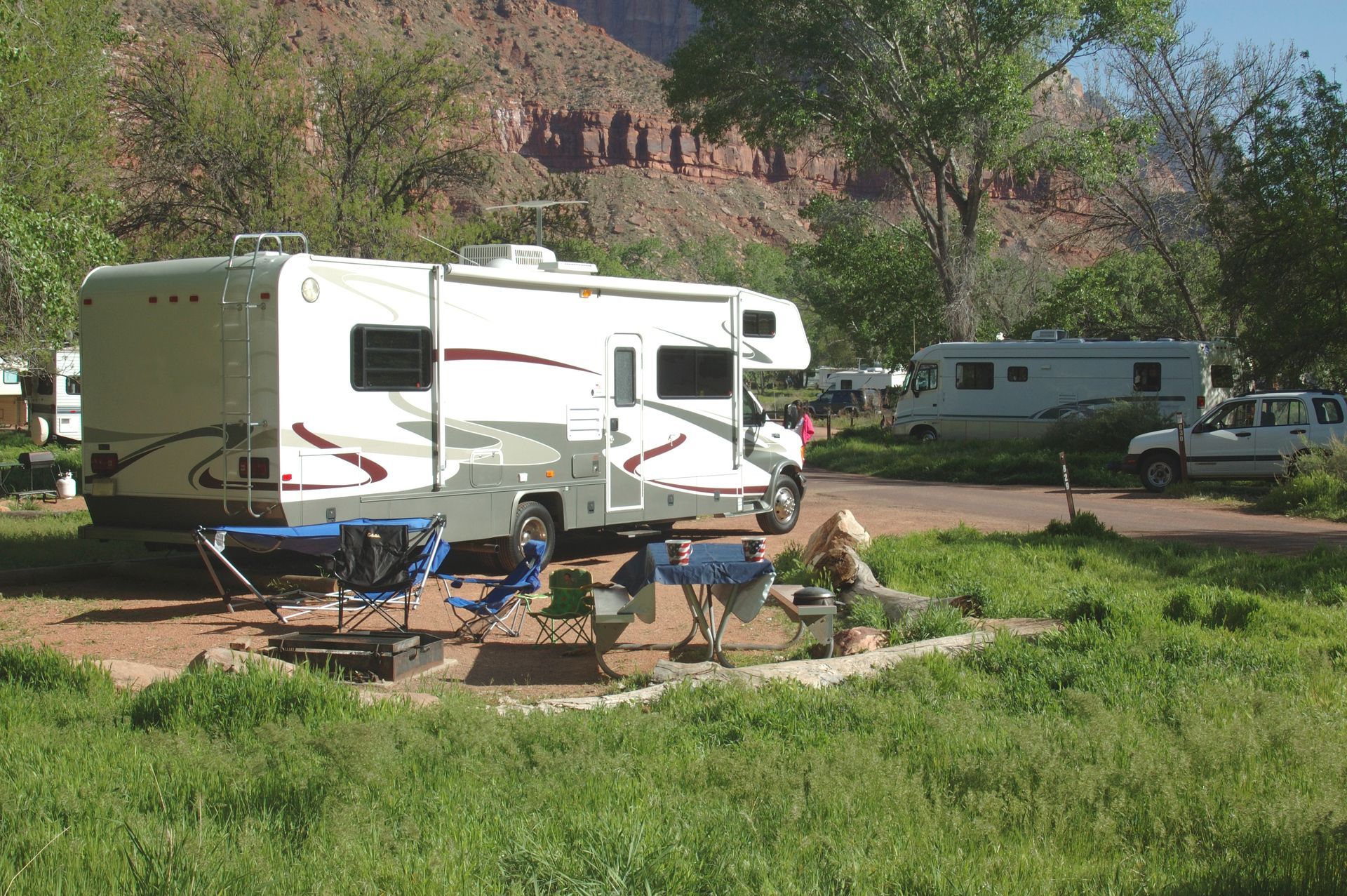 RV campground: motorhomes parked near green grass, with mountains visible in the background.