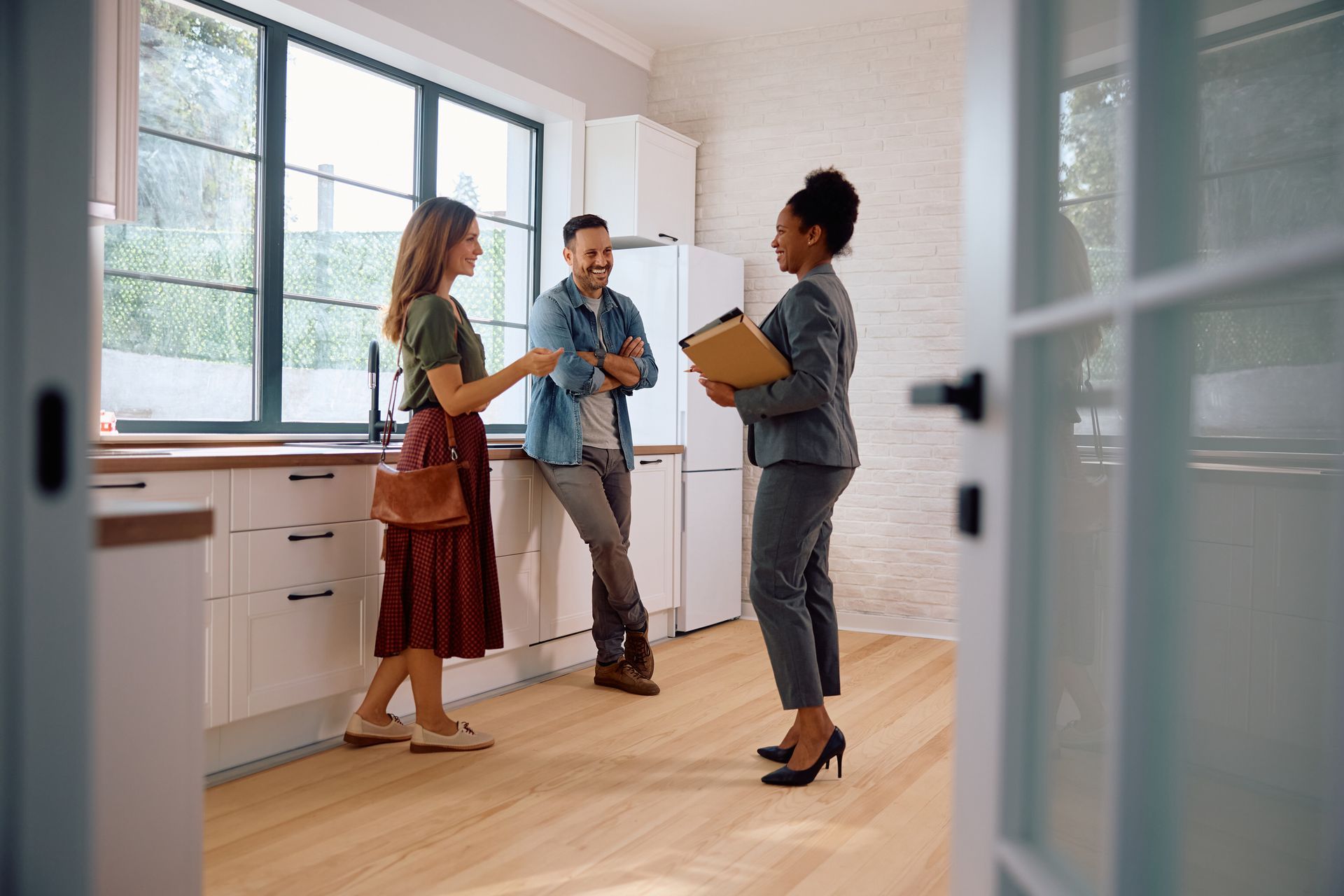 Couple consults with a realtor in a kitchen, discussing details; natural light fills the room.