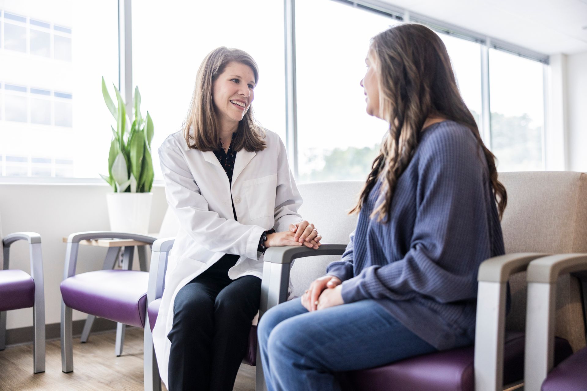 Doctor in a white coat speaking with a patient in a waiting room, both smiling.