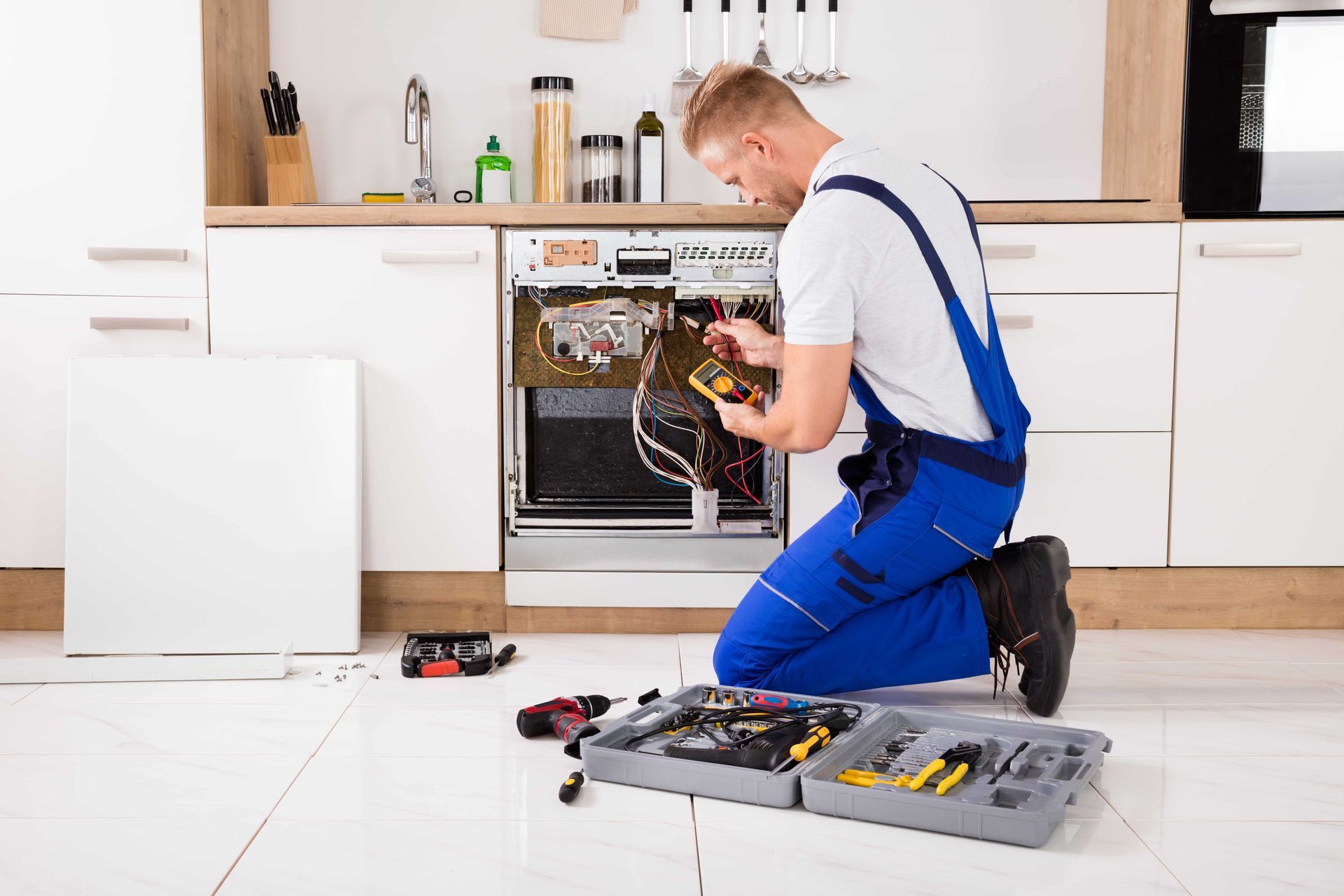 A man is kneeling down in a kitchen fixing a dishwasher.