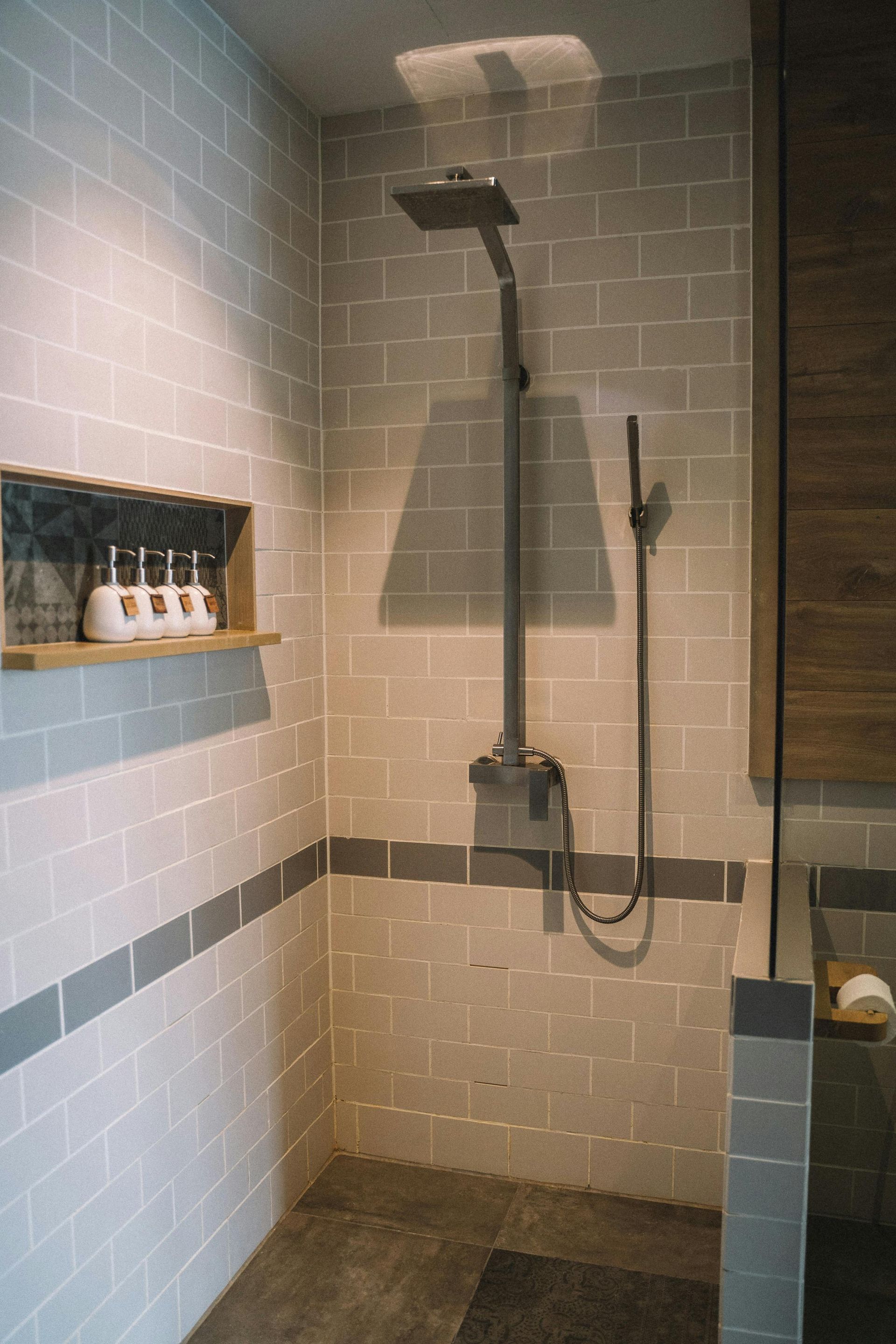 A bathroom with a shower and a shelf with bottles of soap on it.