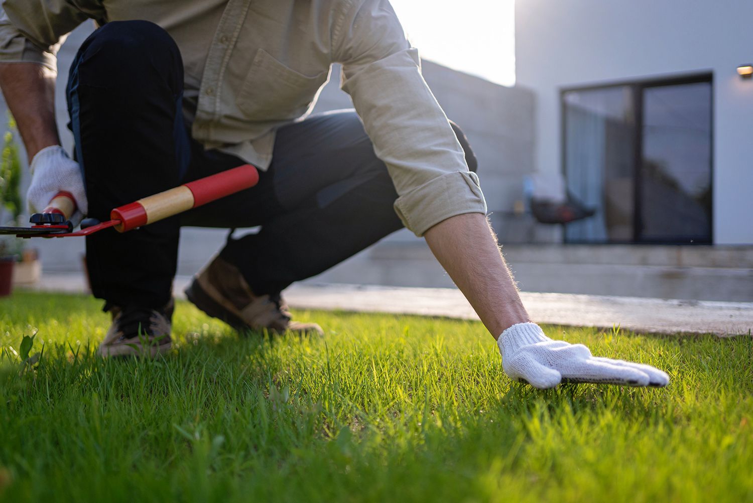 A man is kneeling down in the grass holding a tool.