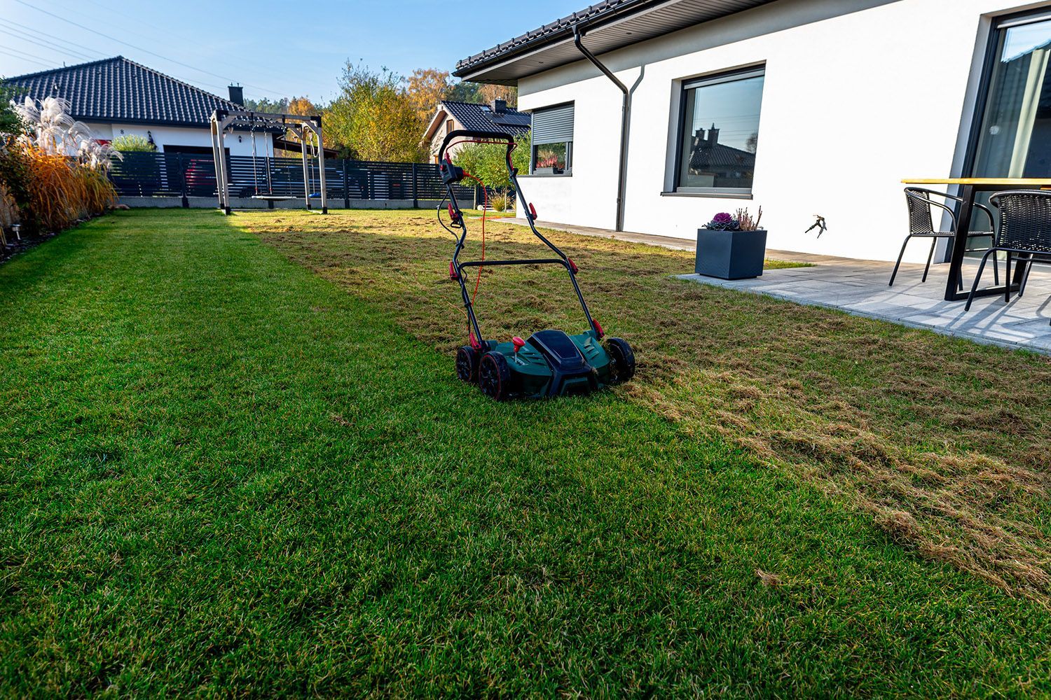 A person is mowing a lush green lawn in front of a house.