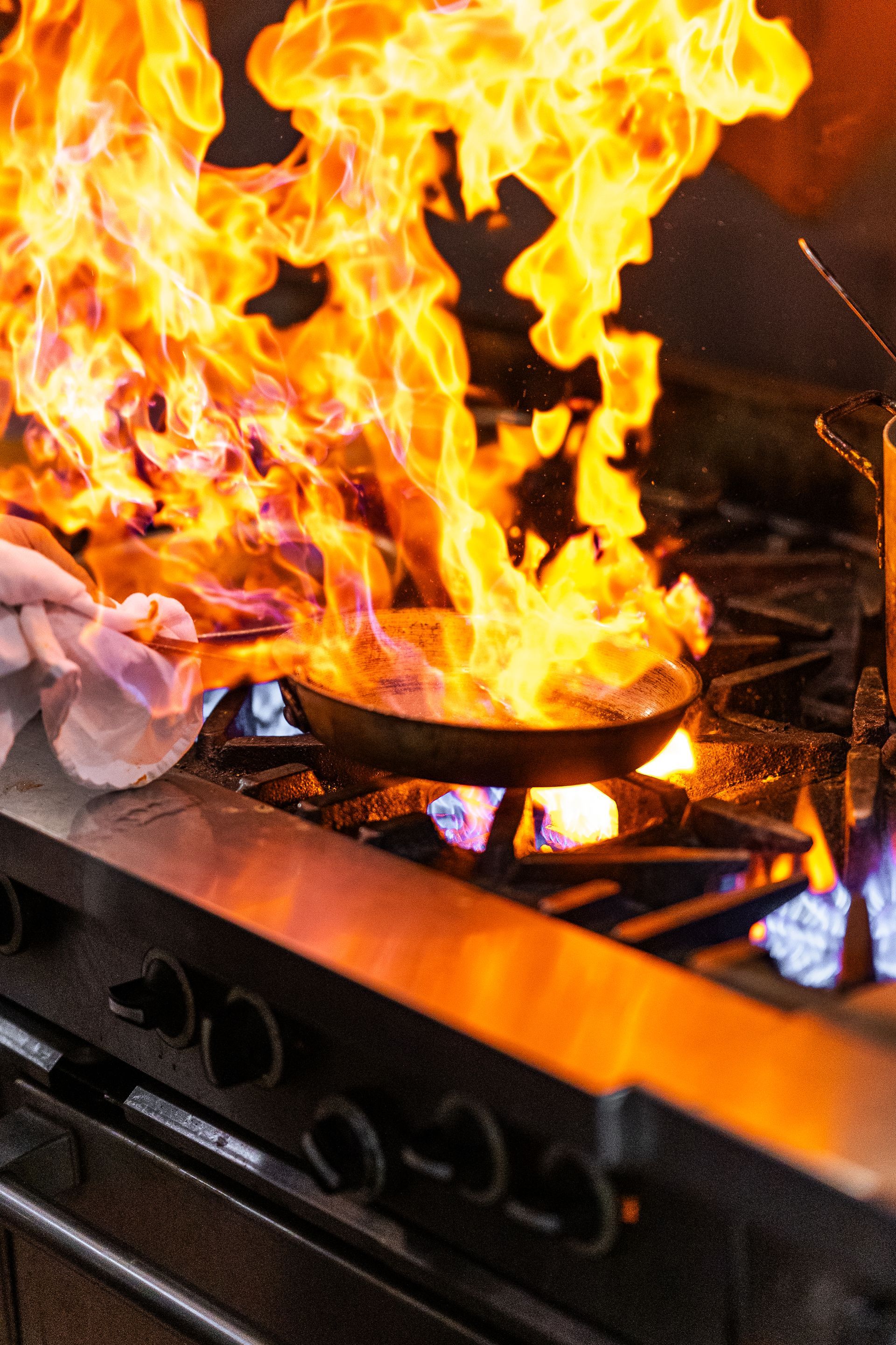 A person is cooking food on a stove with flames coming out of it.