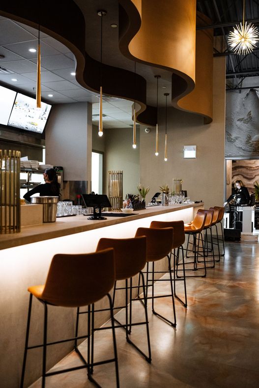 A row of bar stools are lined up in front of a long counter in a restaurant.