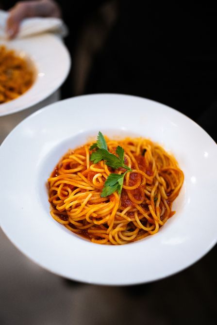 A person is holding a plate of spaghetti with tomato sauce.