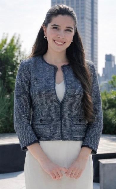 Woman with long brown hair smiles, wearing a burgundy sweater, inside a doorway.