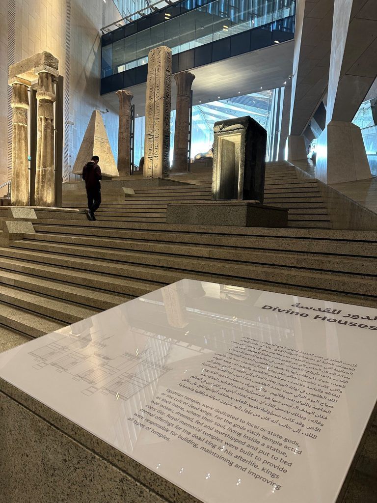 Museum interior with ancient artifacts on display; person walking up steps.