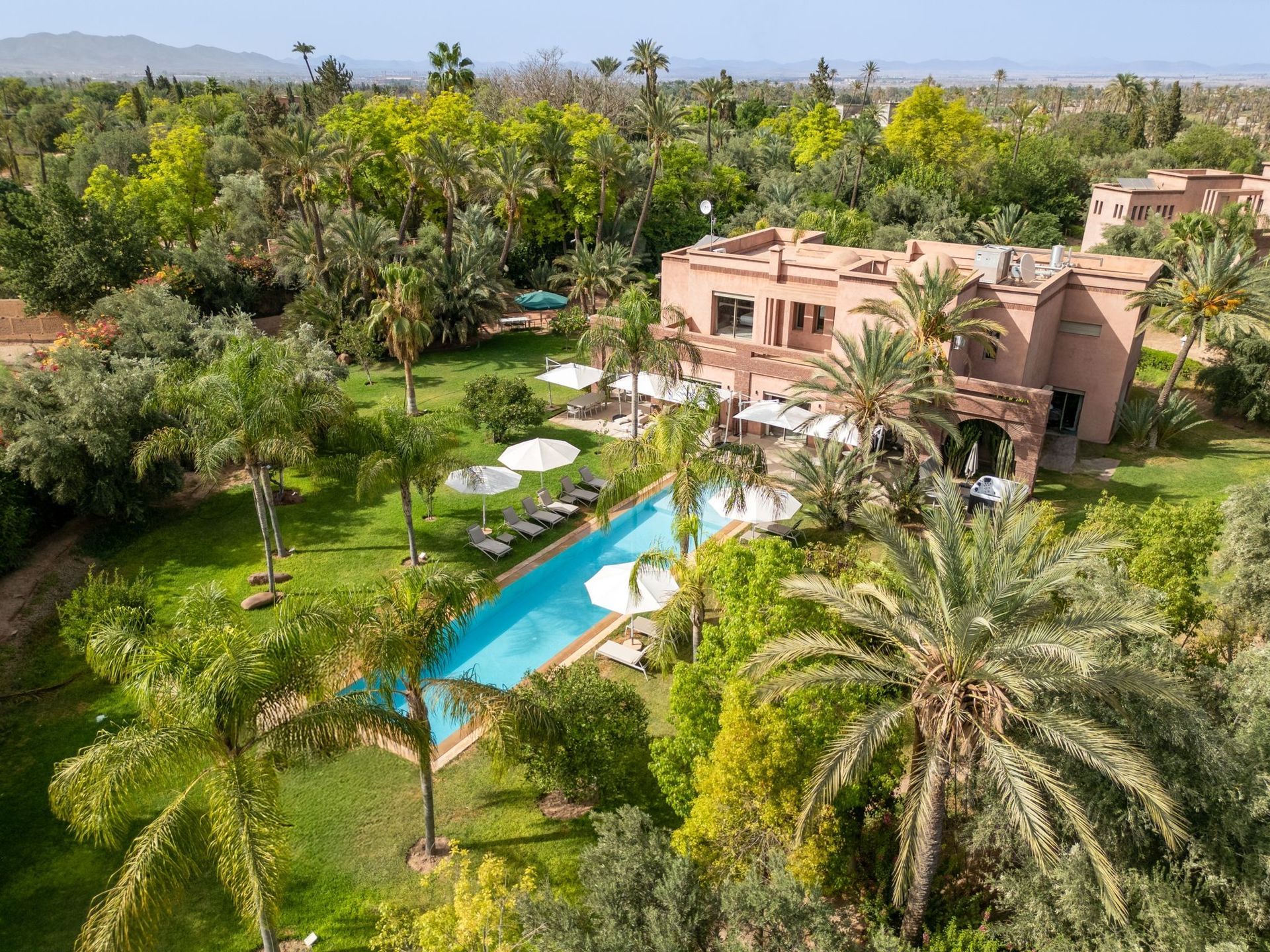 Poolside resort with palm trees, lush greenery, and terracotta buildings in Marrakech, Morocco.