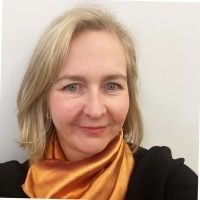 Woman with blonde hair, wearing an orange scarf and black jacket, smiles.