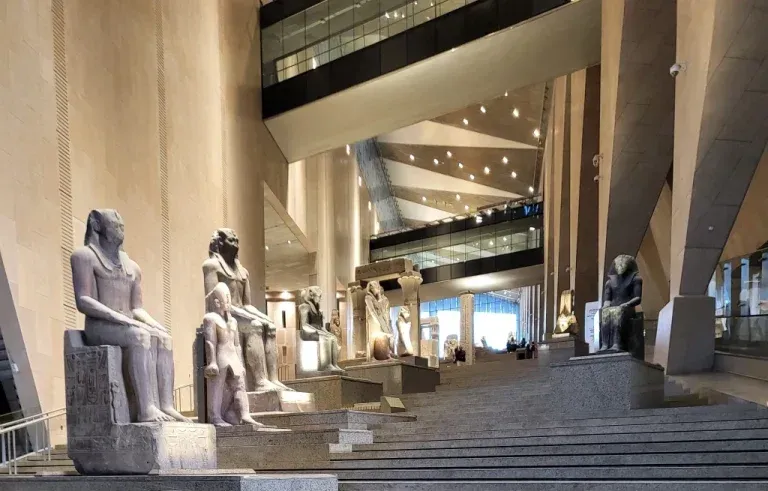 Interior view of the Grand Egyptian Museum with statues along a staircase, featuring modern architecture.