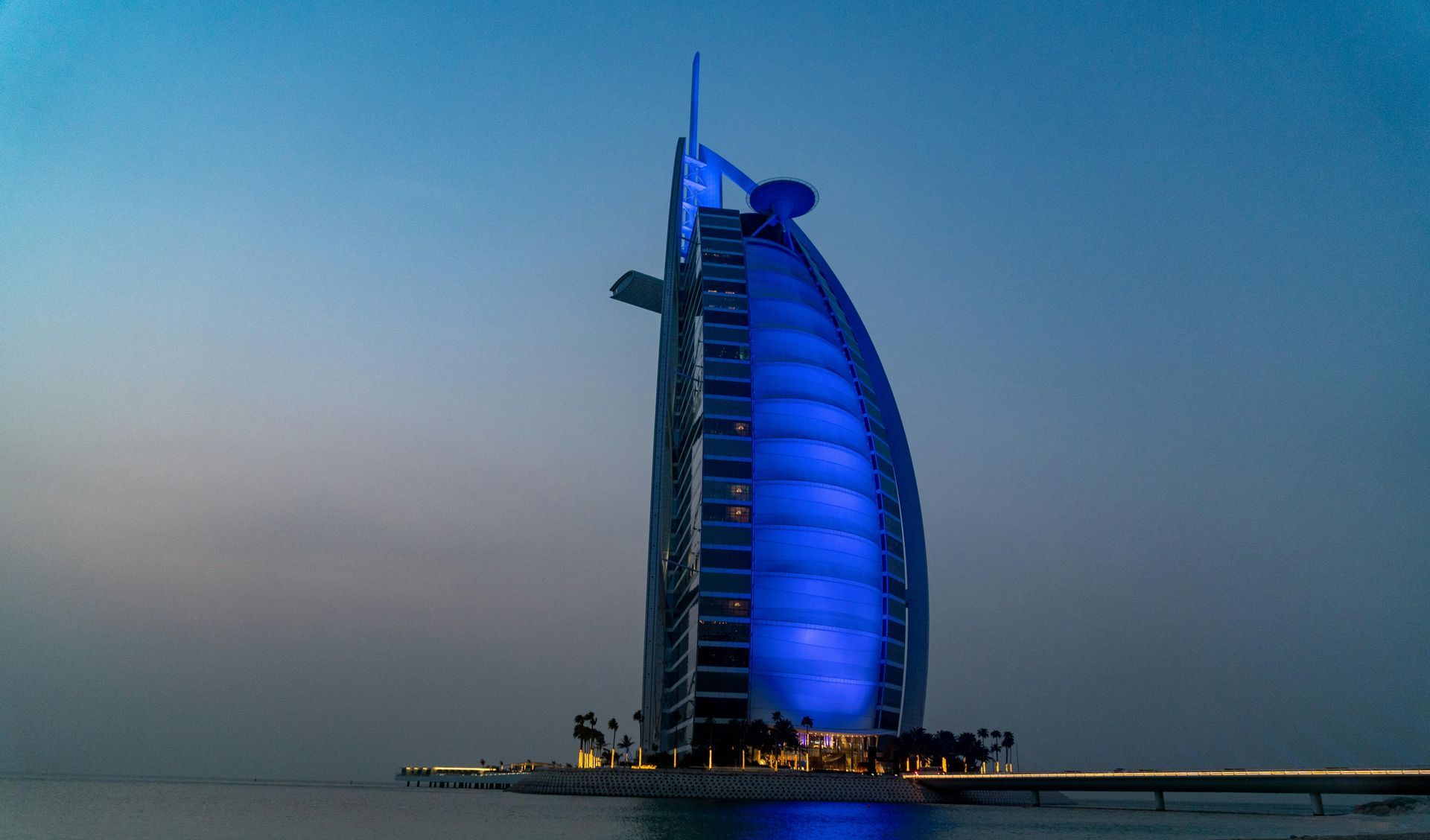 Burj Al Arab hotel in Dubai, illuminated with blue lights, against a dusky sky.