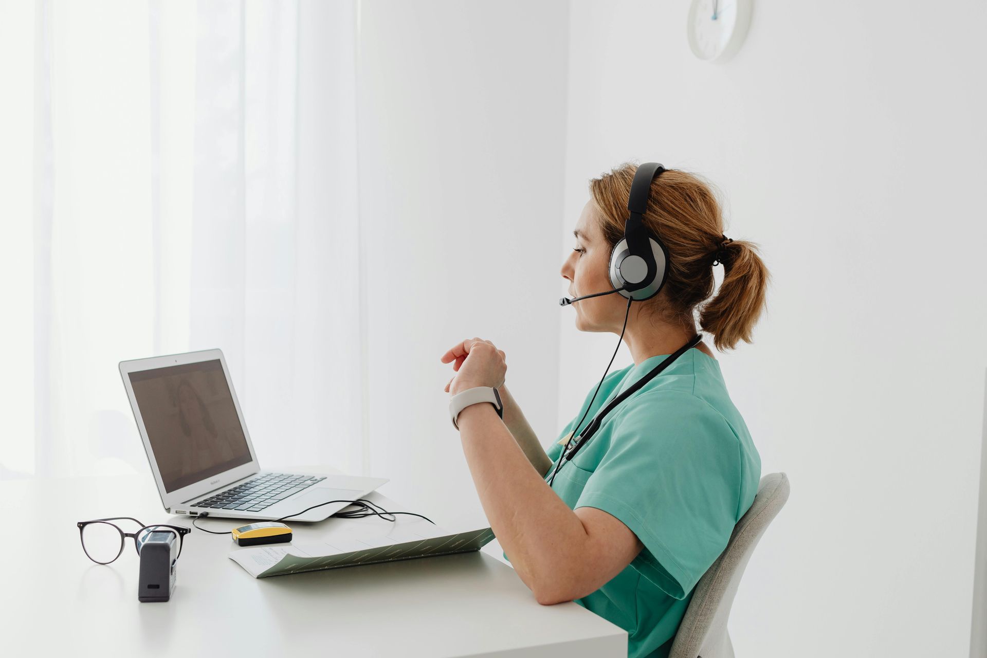 Woman in scrubs with headset and laptop, possibly providing telehealth consultation.