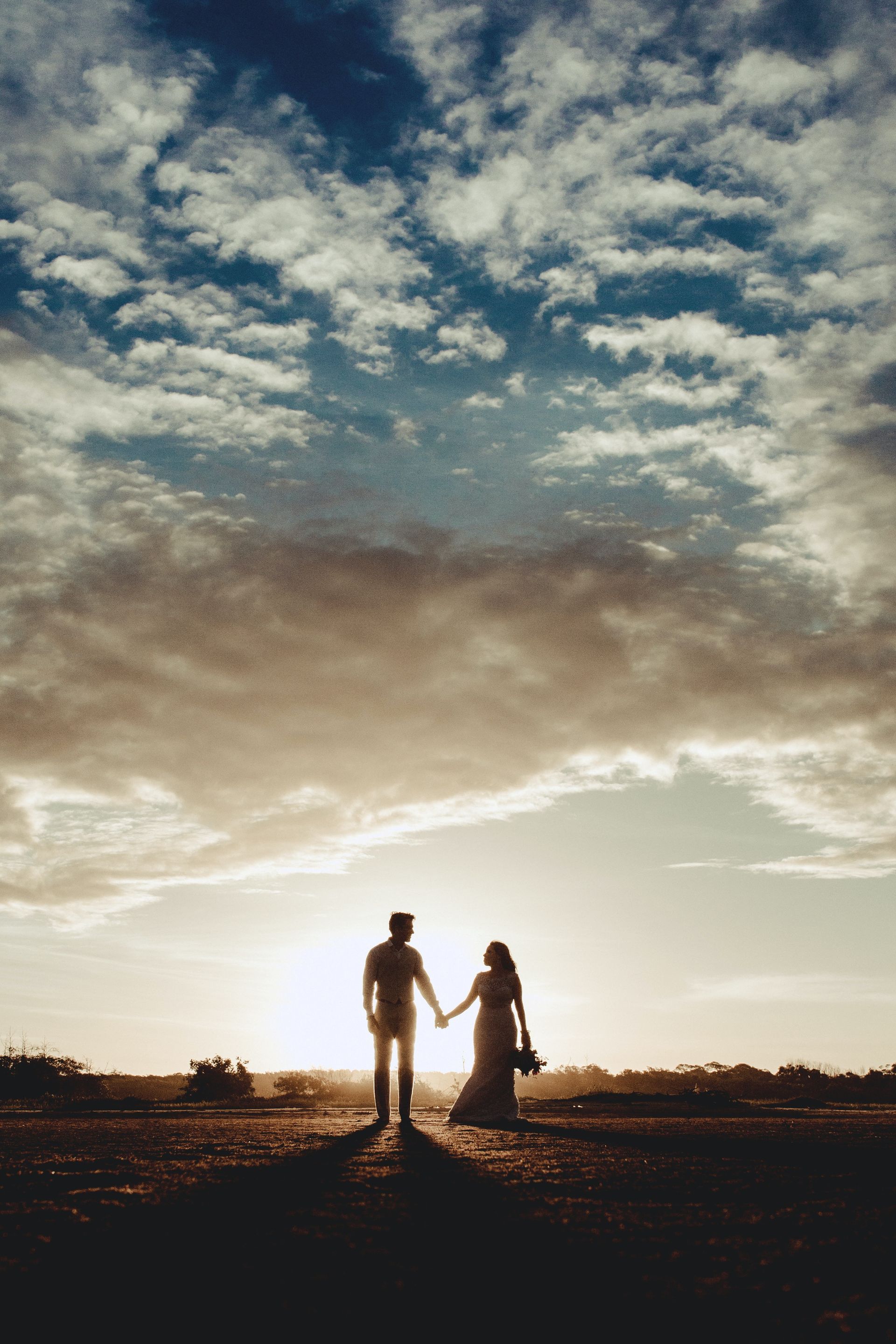 A bride and groom are holding hands while standing in a field at sunset.