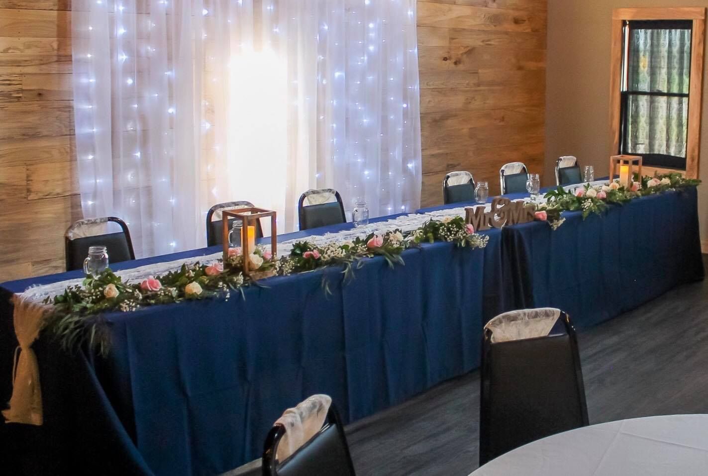 A long table with a blue tablecloth and flowers on it in a room.