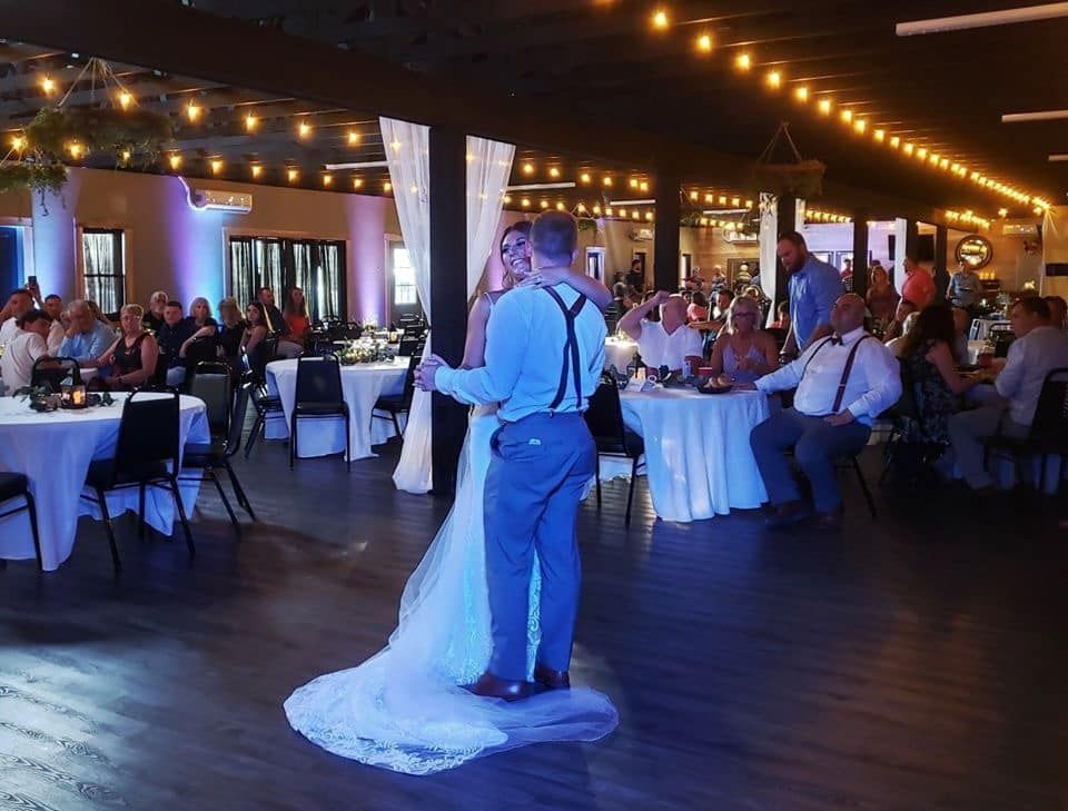 A bride and groom are dancing in a large room at their wedding reception.