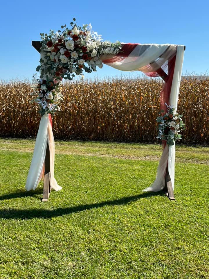 A wooden arch decorated with flowers is sitting in the middle of a grassy field.