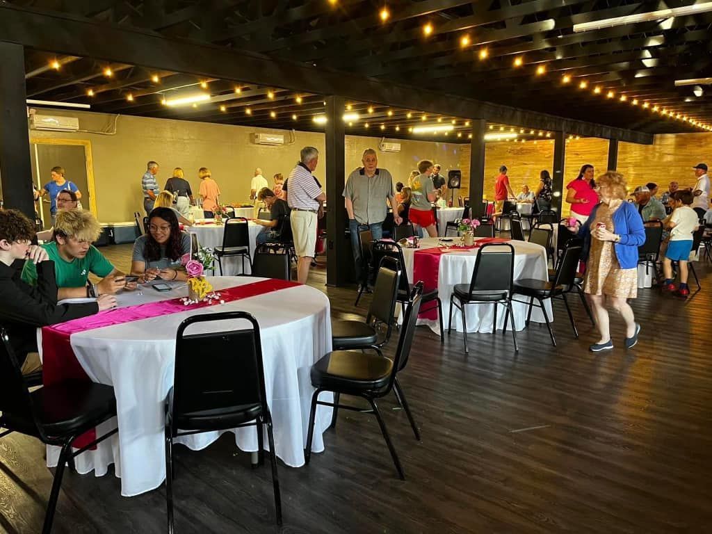 A large room filled with tables and chairs and people standing around.