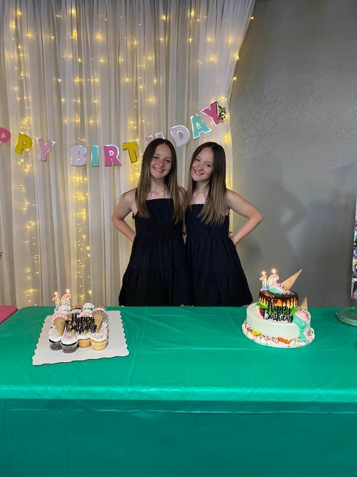 Two girls are standing next to a birthday cake on a table.