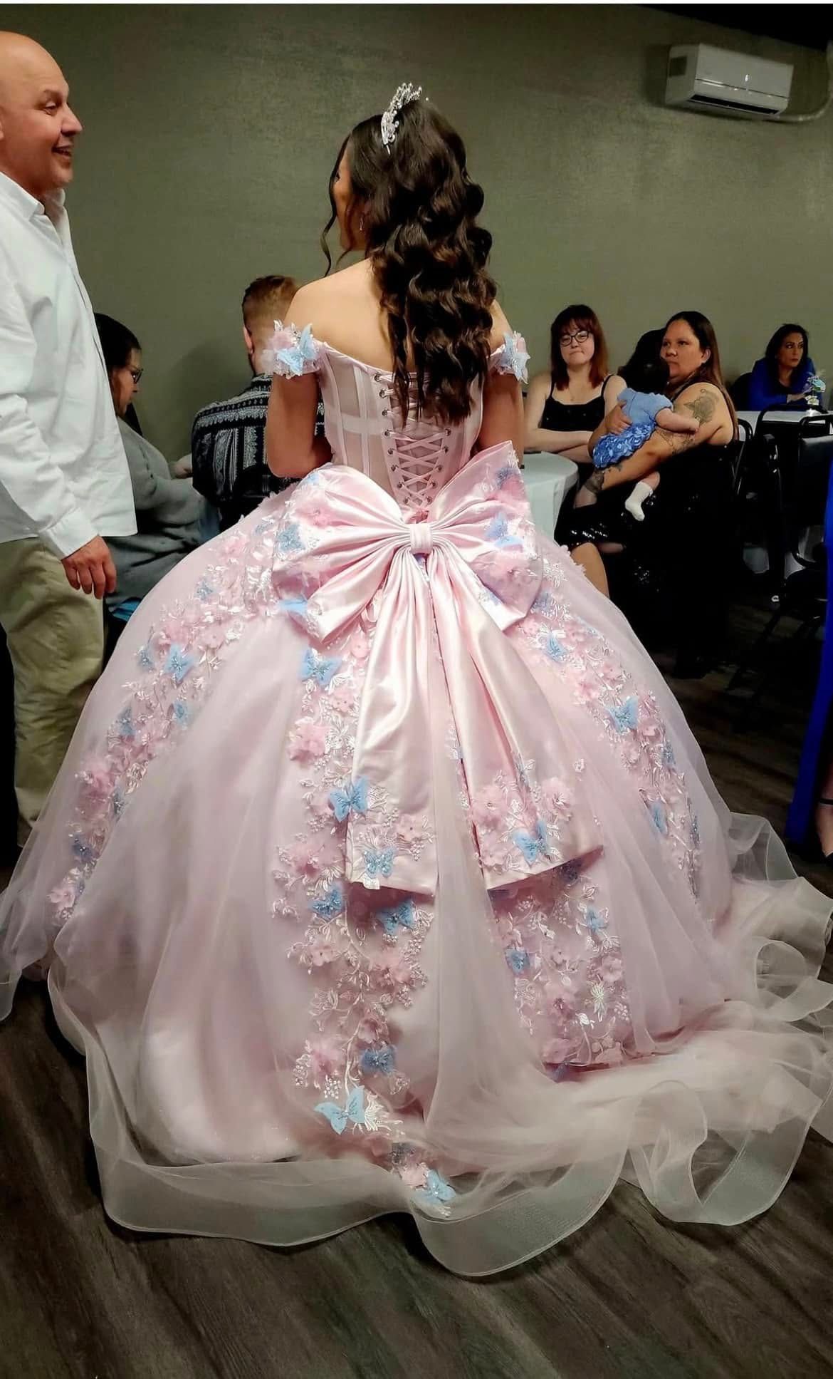 A woman is wearing a pink ball gown with a bow on the back.