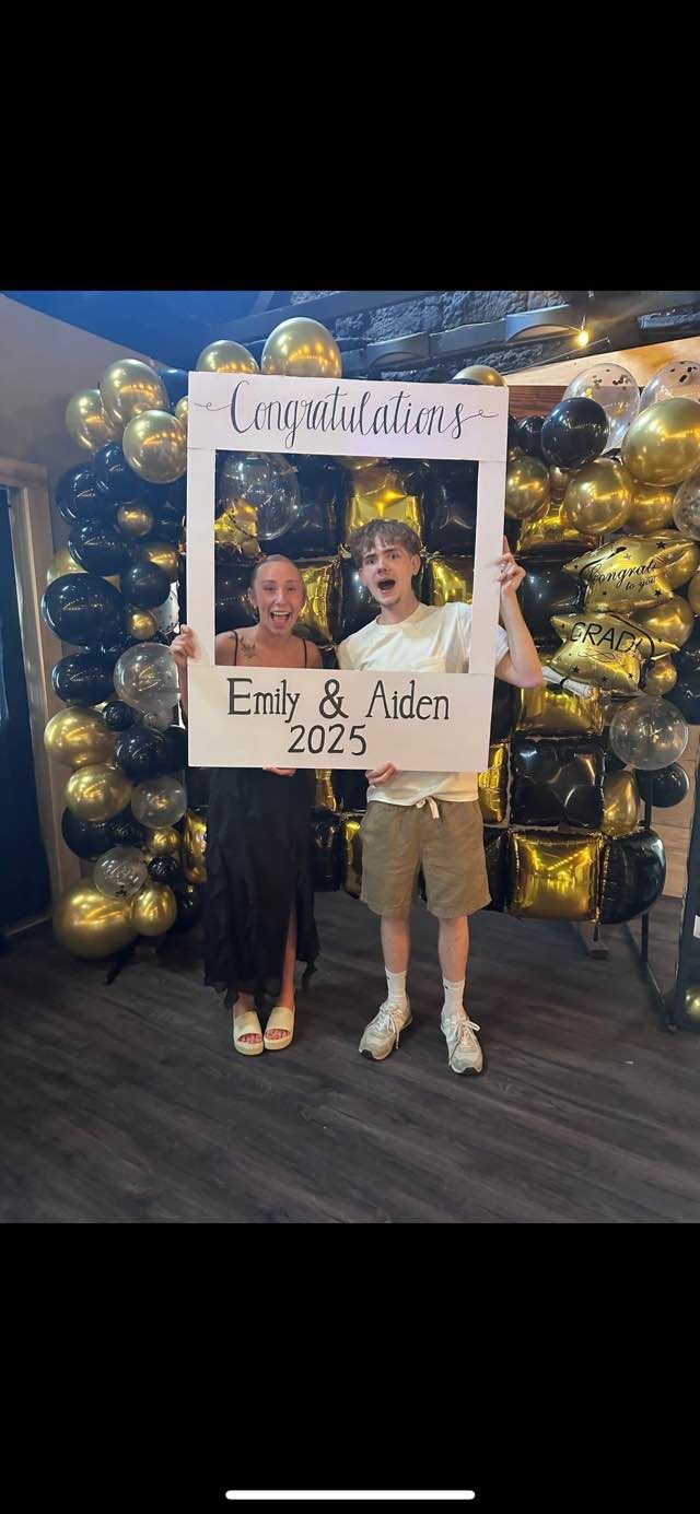 A man and a woman are holding a picture frame in front of balloons.